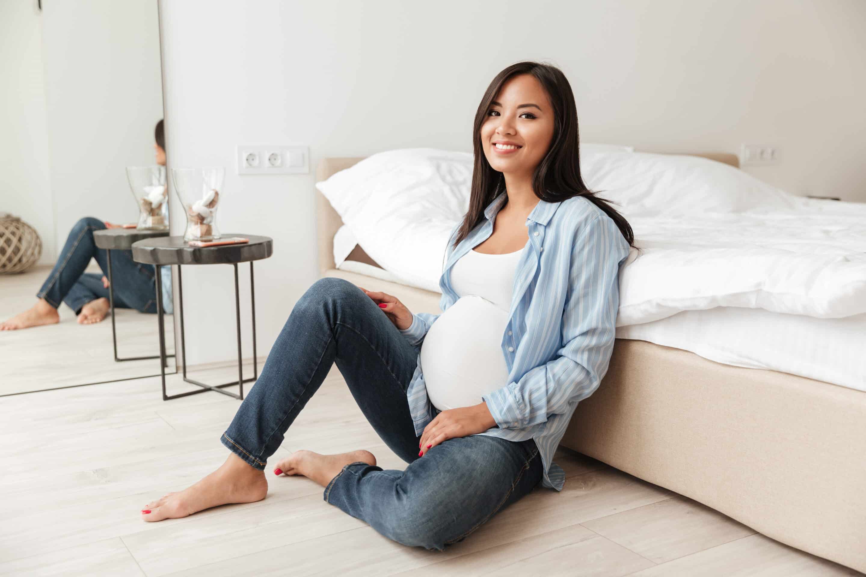 smiling pregnant woman sitting on the floor by her bed, making pregnancy friends