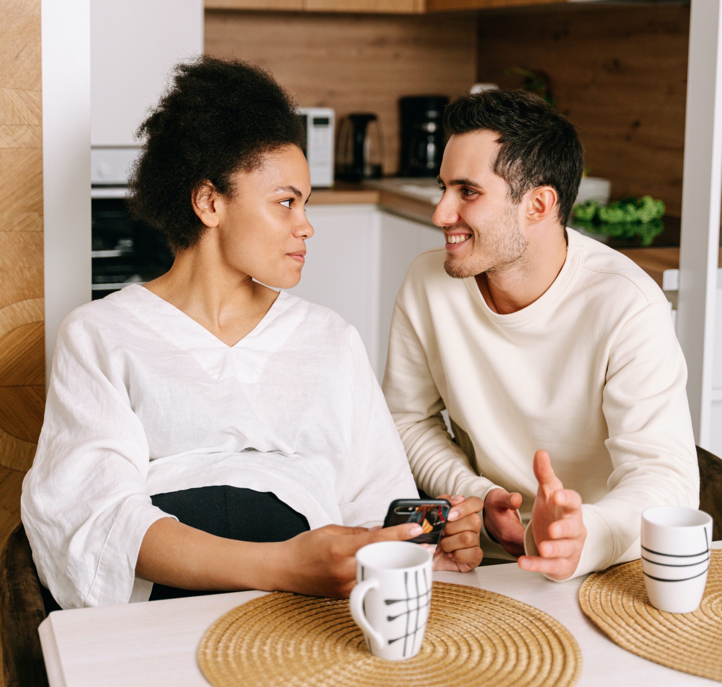 expectant couple sitting at a table talking over cups of tea and coffee, expecting a baby