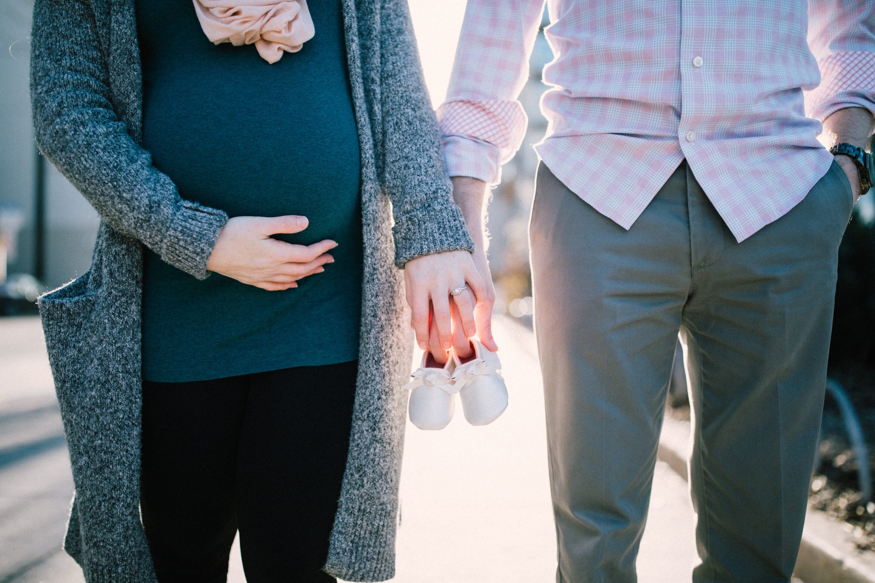 Body shot of an expectant couple holding hands with baby booties, saving for baby's future