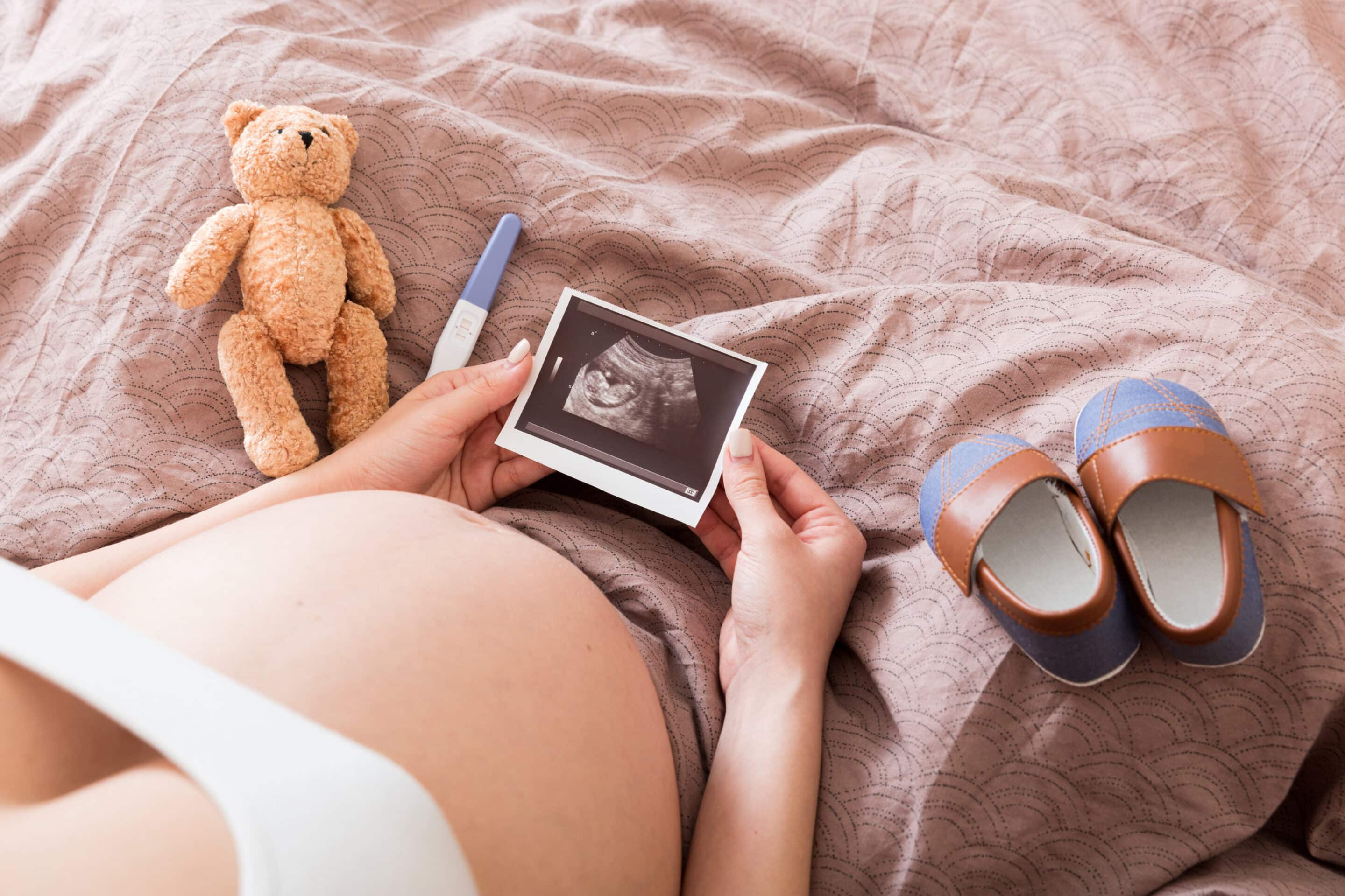 Pregnant Woman sitting on bed and Looking At Ultrasound Scan photo of her Baby.