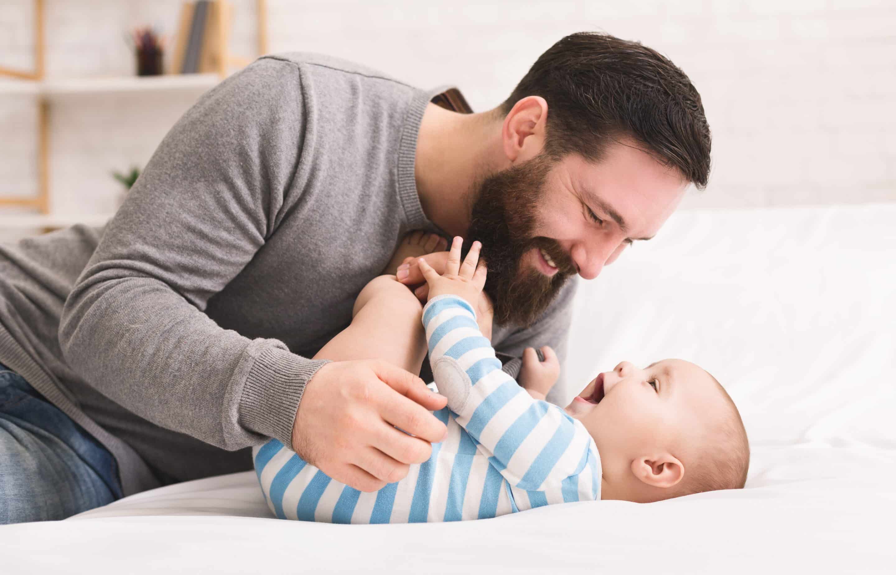 A father plays with his laughing child on a bed.