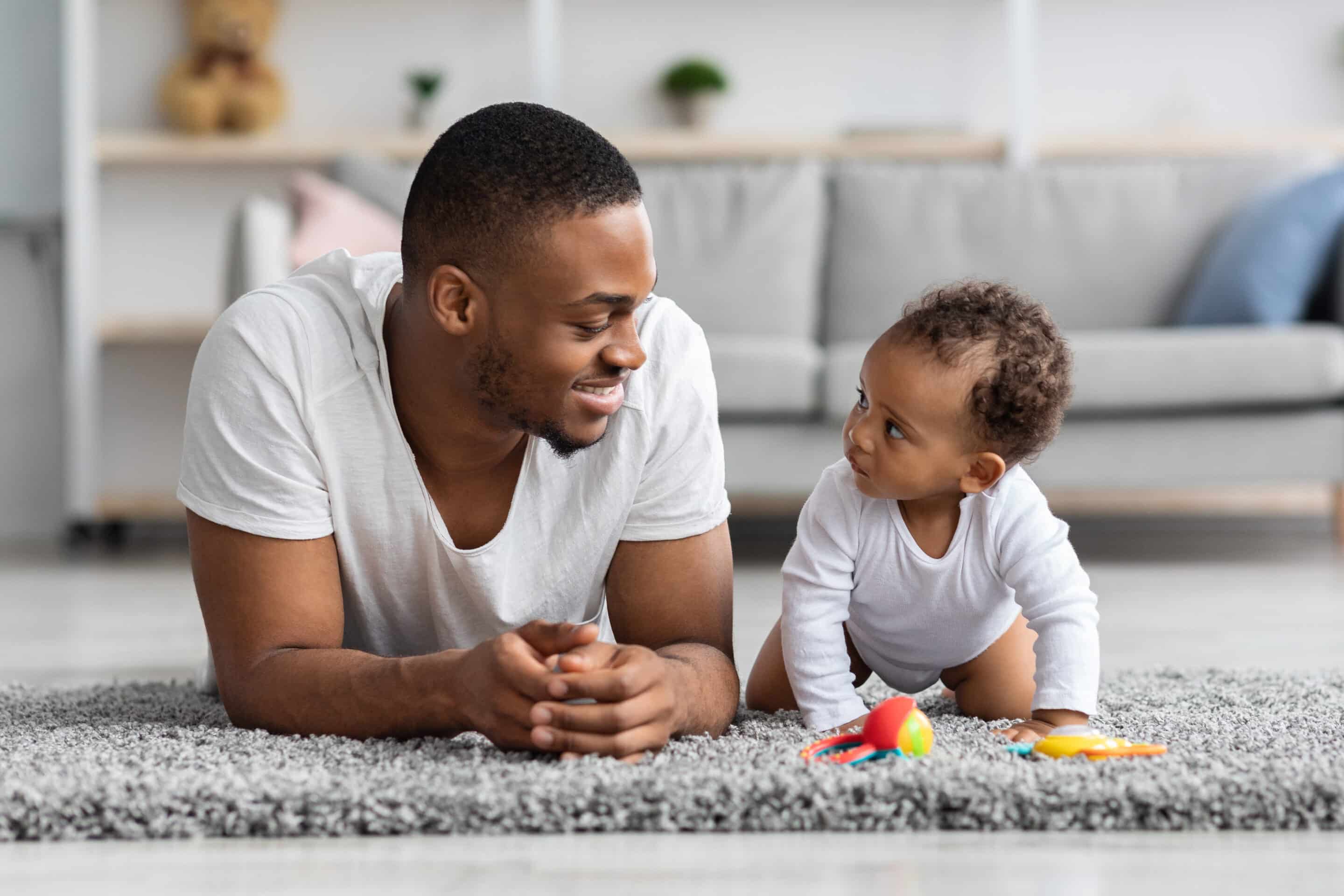 A dad and son lay facing each other on a rug. Blog for paternity leave